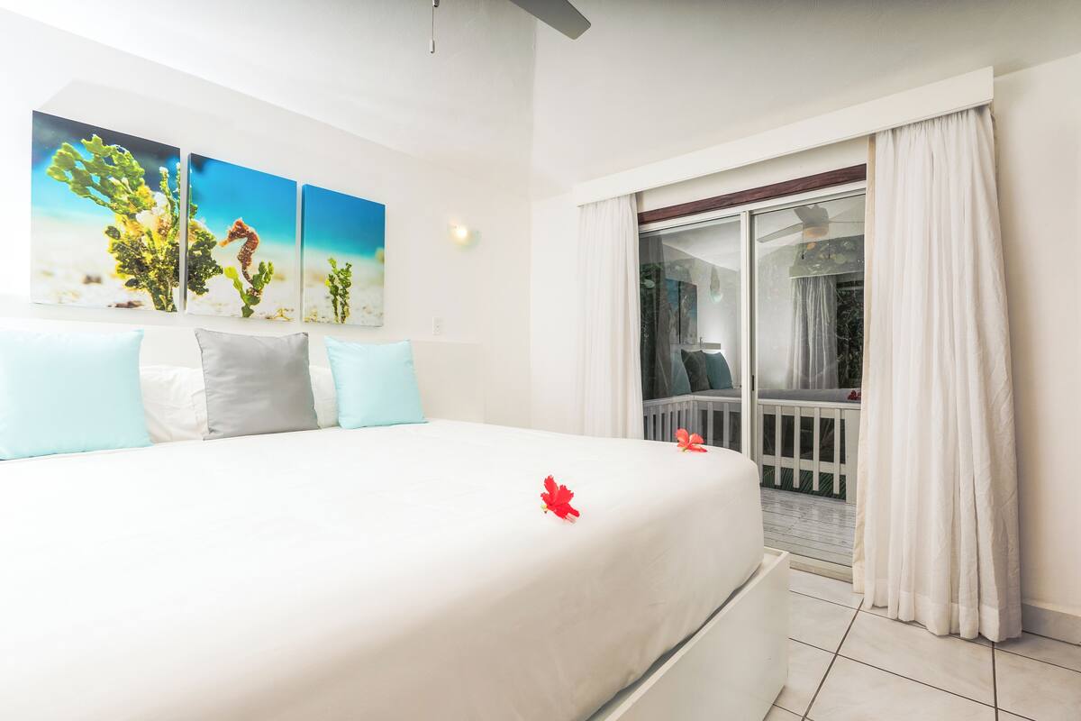 Habitación de hotel con una cama, un balcón con vistas y un cuadro en la pared.