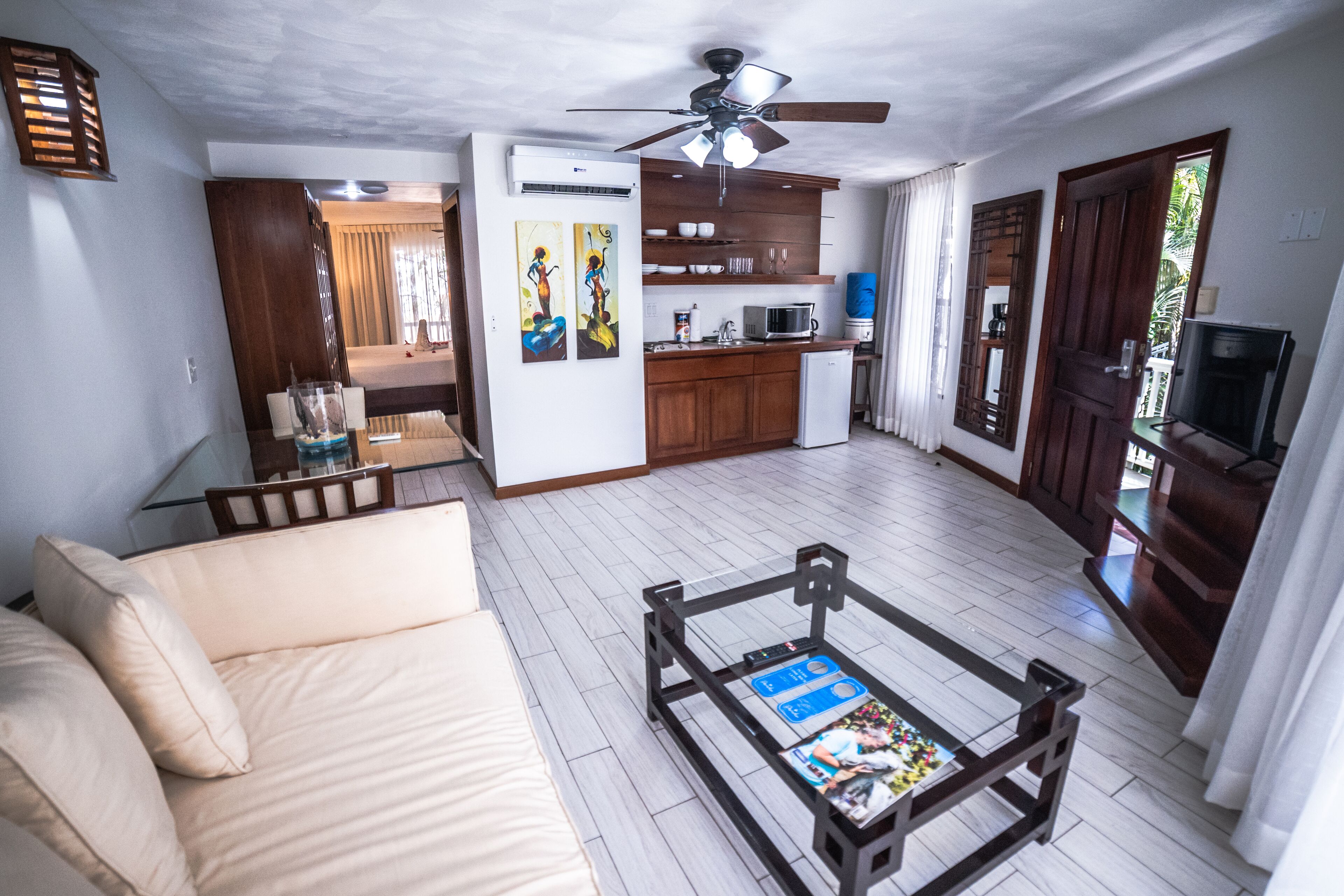 A compact living space with a sofa, a coffee table, a ceiling fan, a kitchenette, and a TV.