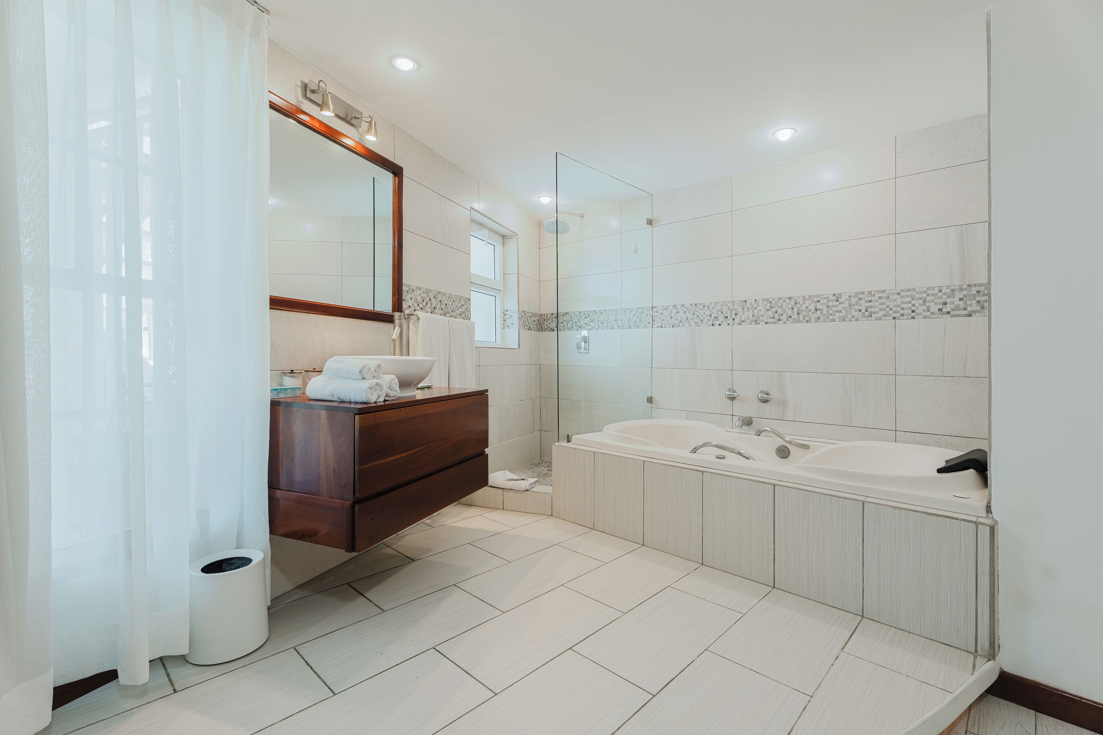 Un bagno moderno con uno specchio grande, un mobile bagno in legno, una vasca e una doccia.