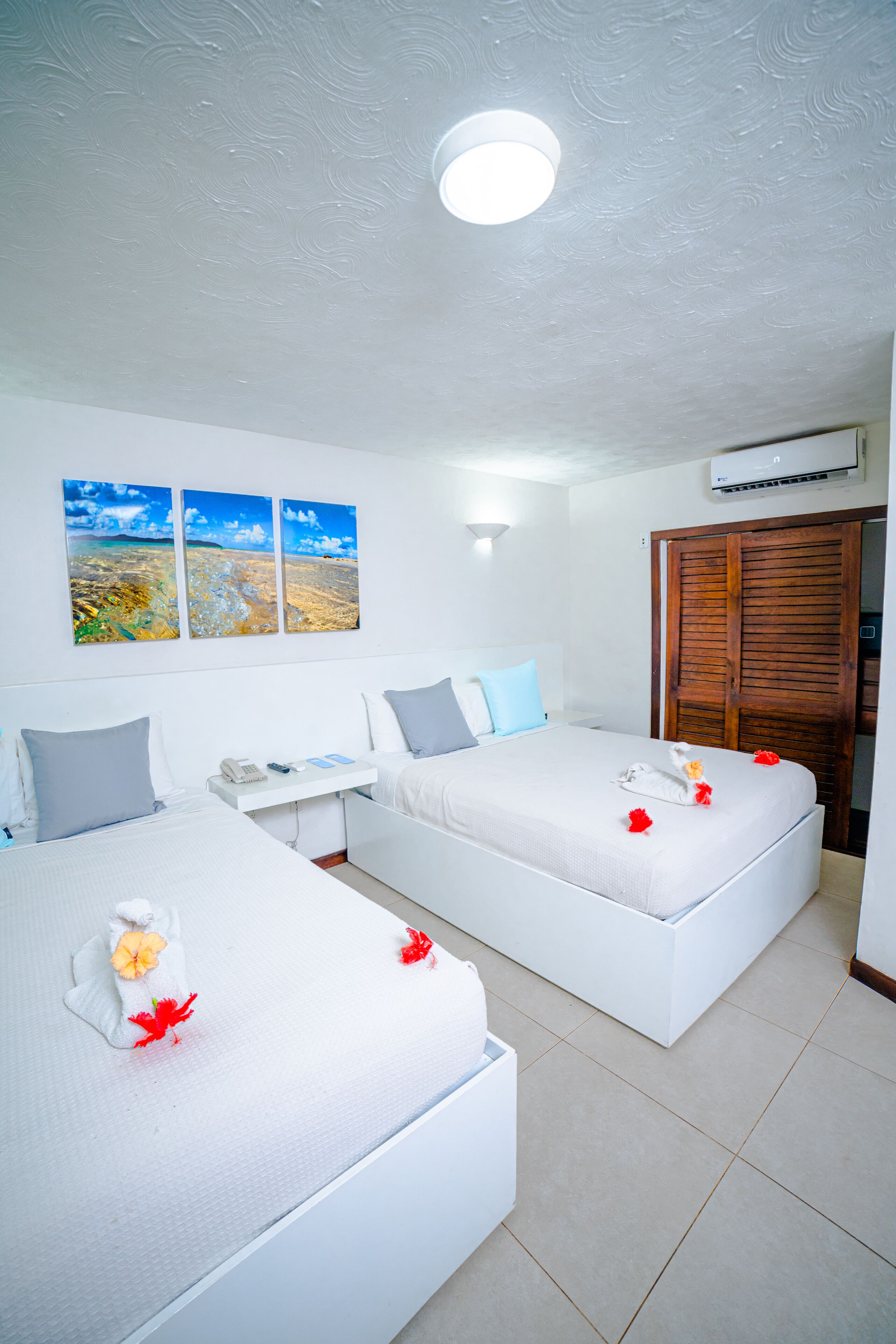 Habitación de hotel con dos camas, un escritorio pequeño, un armario y tres cuadros de paisajes en la pared.
