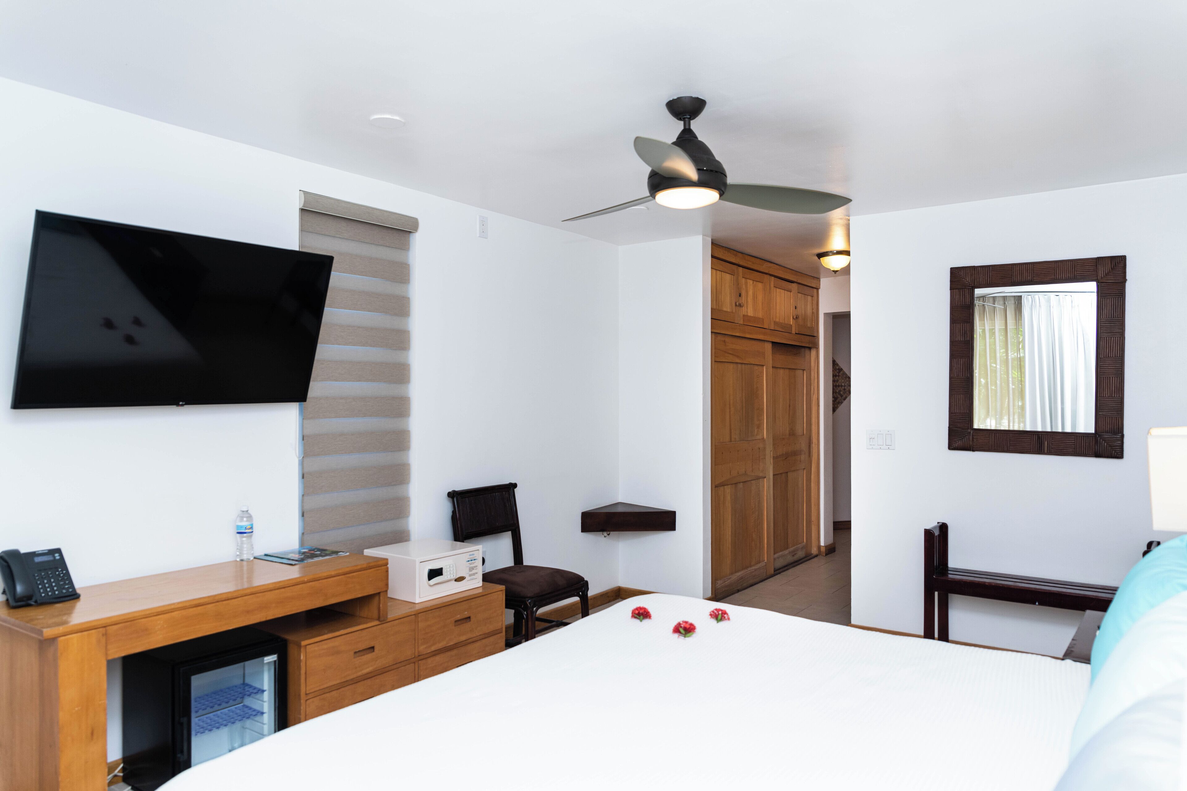 Ein Hotelzimmer mit einem Bett, einem Schreibtisch mit Computer, einem an der Wand befestigten Fernseher, einem Deckenventilator und einem Holzschrank.