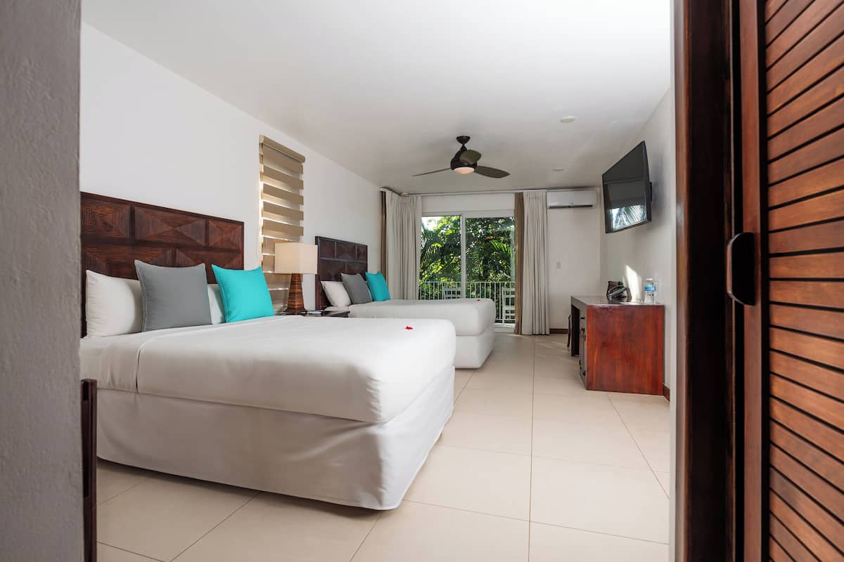 Habitación de hotel con dos camas, cabecera de madera, televisión y vista a áreas verdes.