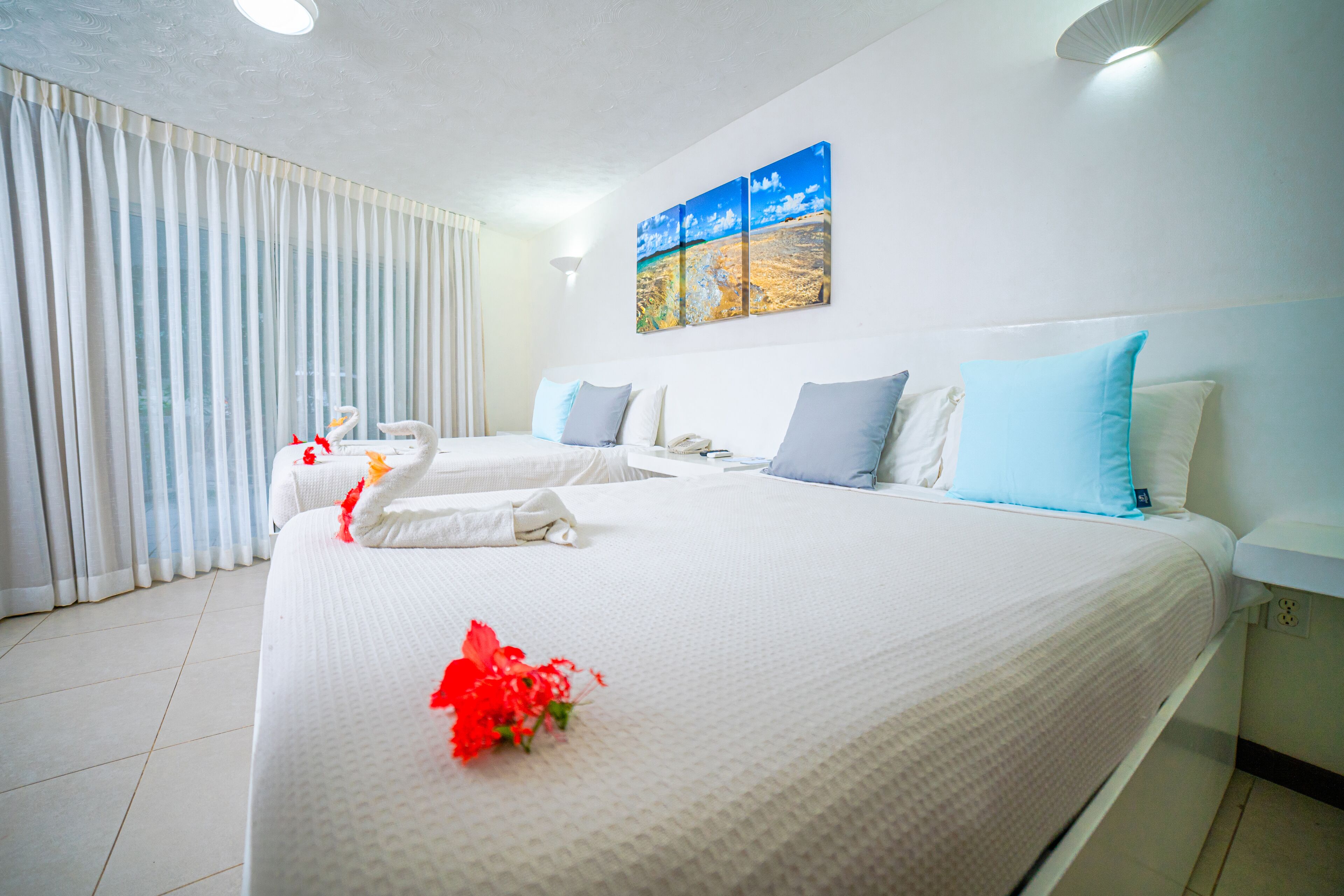 Habitación de hotel con dos camas, ropa de cama blanca, un cuadro en la pared y una ventana con cortinas.
