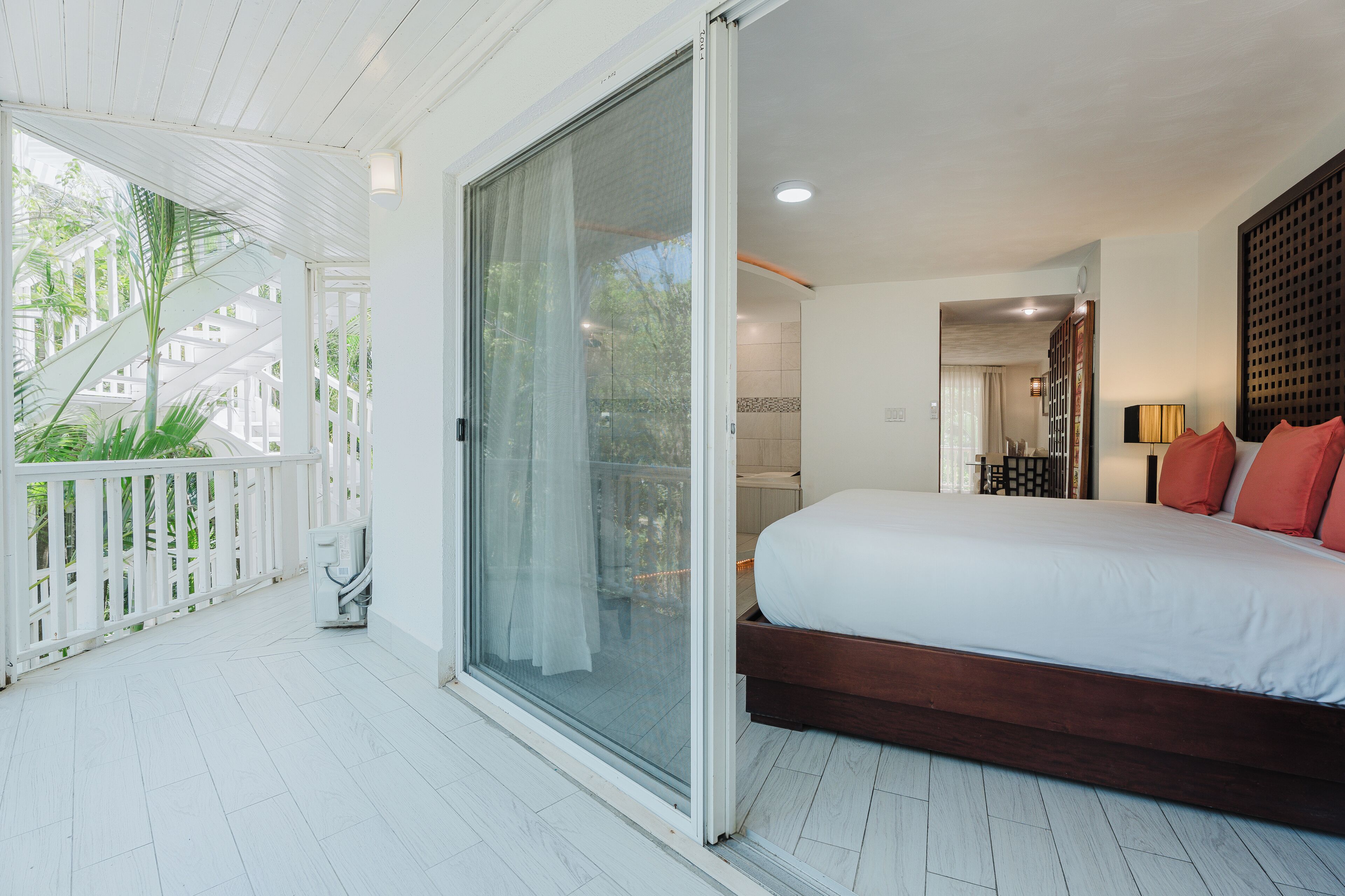 A bedroom with a large bed, a sliding glass door leading to a balcony, and a view of the outdoors.