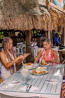 Un comedor con techo de paja, asientos al aire libre y una mesa con bebida y comida.