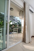 Un balcón con una silla blanca, un ventanal de vidrio y vistas a palmeras.