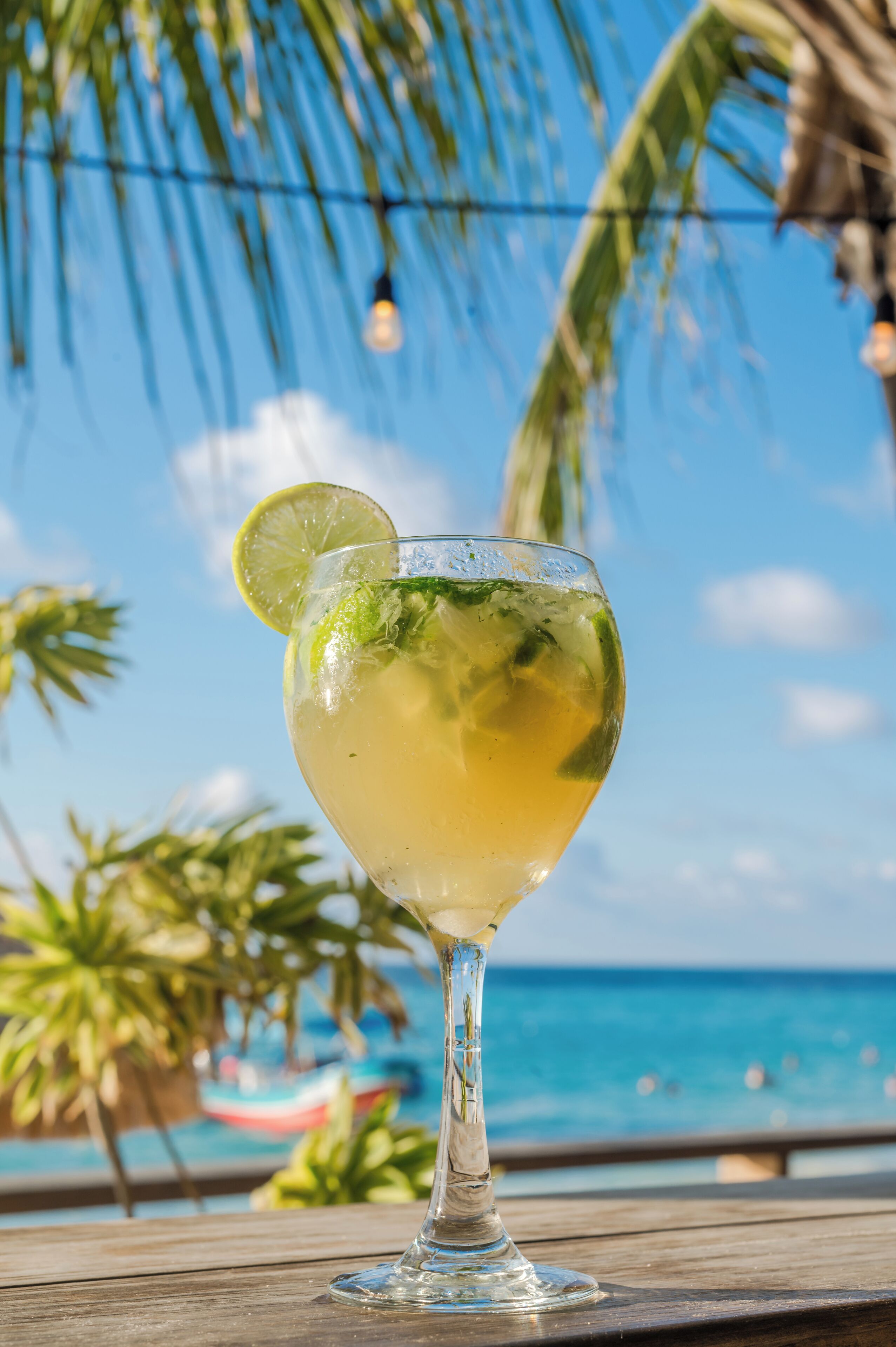 A cocktail glass with a lime slice on a wooden table by the beach.