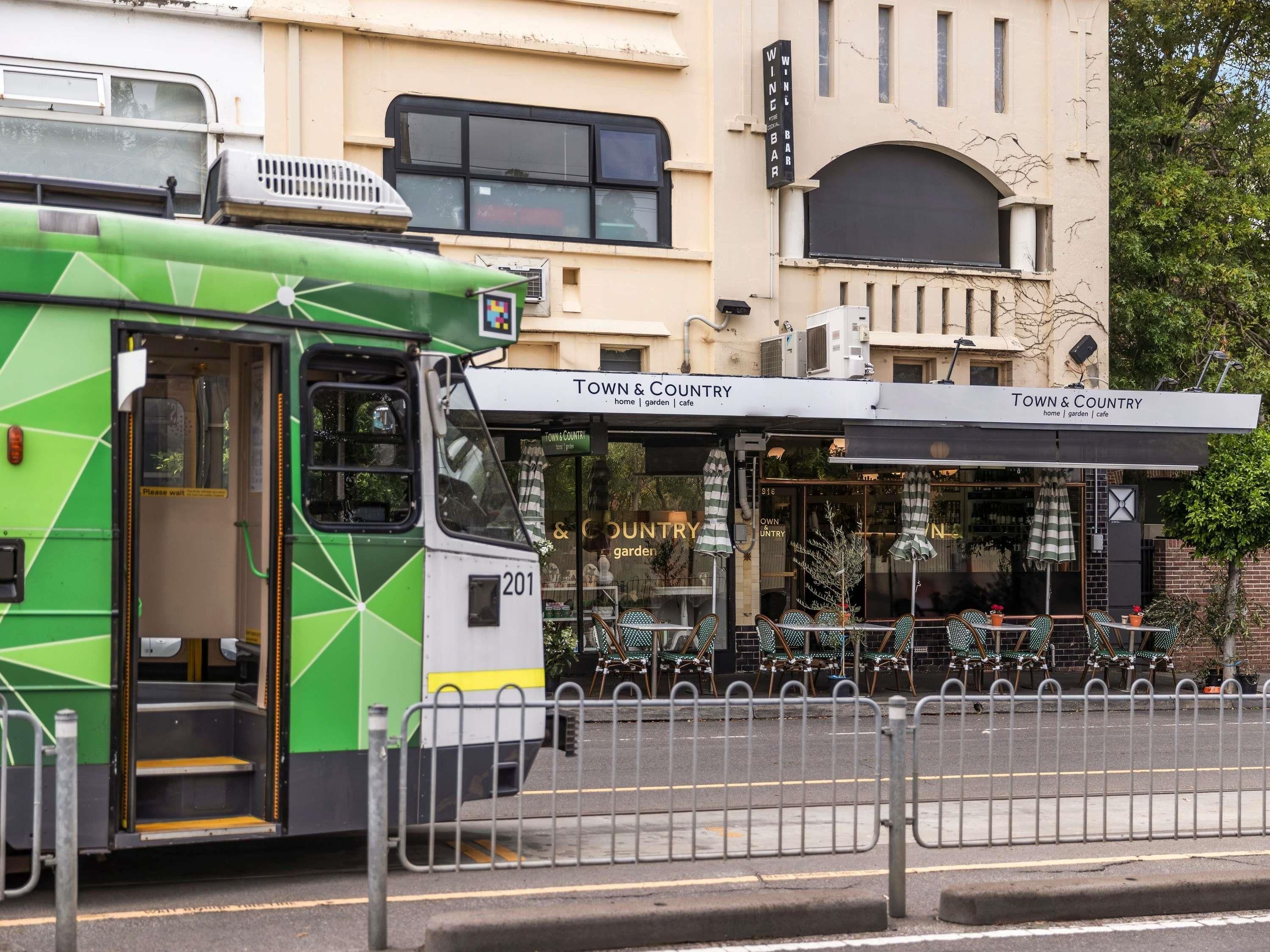 Een groene bus geparkeerd voor een gebouw met een bord waarop 'Town & Country' staat, plus terrasplekken.