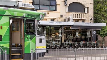 Un autobús verde estacionado frente a un edificio con un letrero que dice 'Town & Country' y terraza al aire libre.