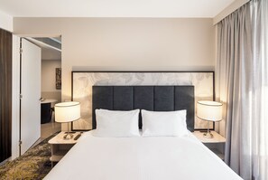 A hotel room with a large bed, two bedside lamps, a headboard with leaf patterns, and a view of a bathroom.