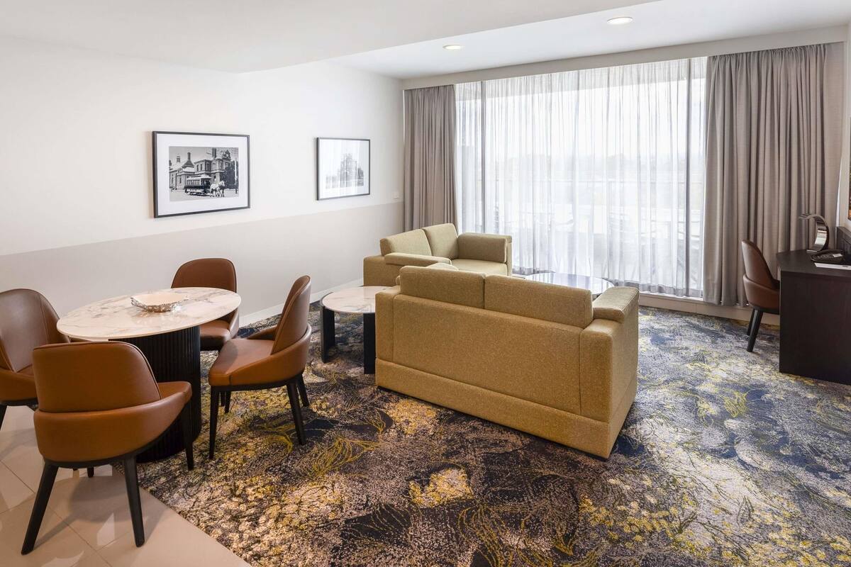 Habitación de hotel con sofá, sillas, una mesita y un escritorio. Hay dos cuadros en la pared.