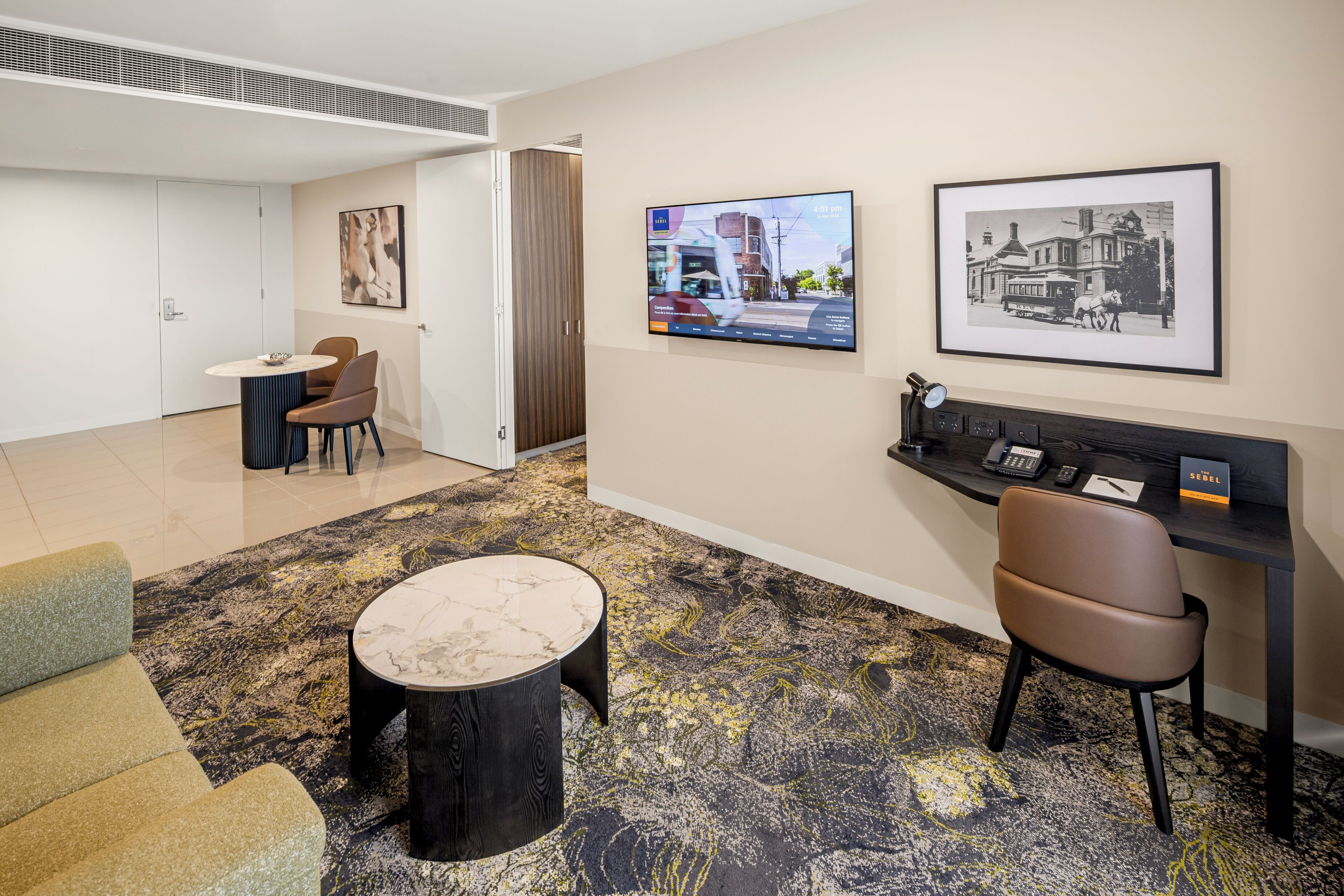 A hotel lobby with a reception desk, seating area, artwork on the walls, and a television screen.