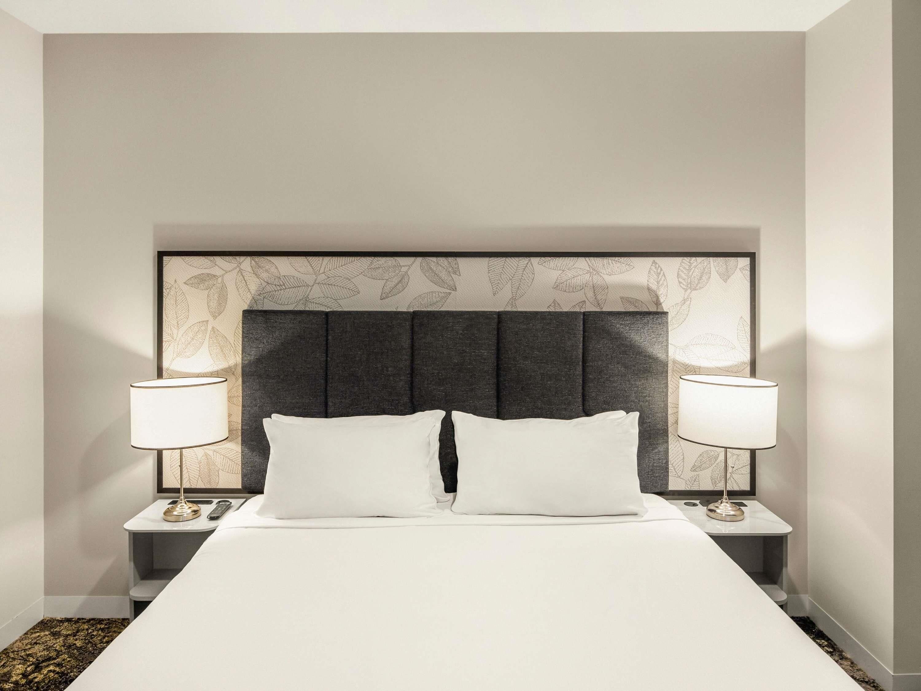 A hotel room with a large bed, two bedside tables, and a headboard with a leaf pattern.
