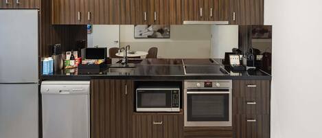 A modern kitchen with wood paneling, a built-in dishwasher, a microwave, an oven, and a stainless steel refrigerator.