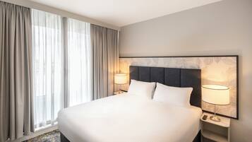 A hotel room with a large bed, two bedside tables with lamps, a window with curtains, and a wall with a leaf pattern.