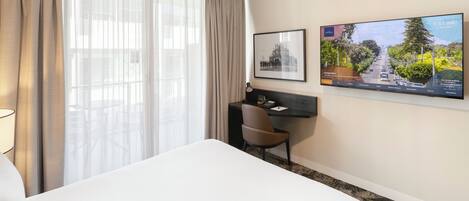 A hotel room with a bed, a desk, a chair, a TV, and a window with curtains.