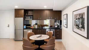 A modern kitchen with dark wood cabinets, a stainless steel refrigerator, and a dining area with a marble table and leather chairs. - The Sebel Melbourne Kew (Kew)