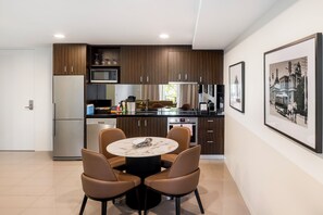 Cozinha moderna com armários de madeira escura, geladeira de aço inoxidável e área de jantar com mesa de mármore e cadeiras de couro.