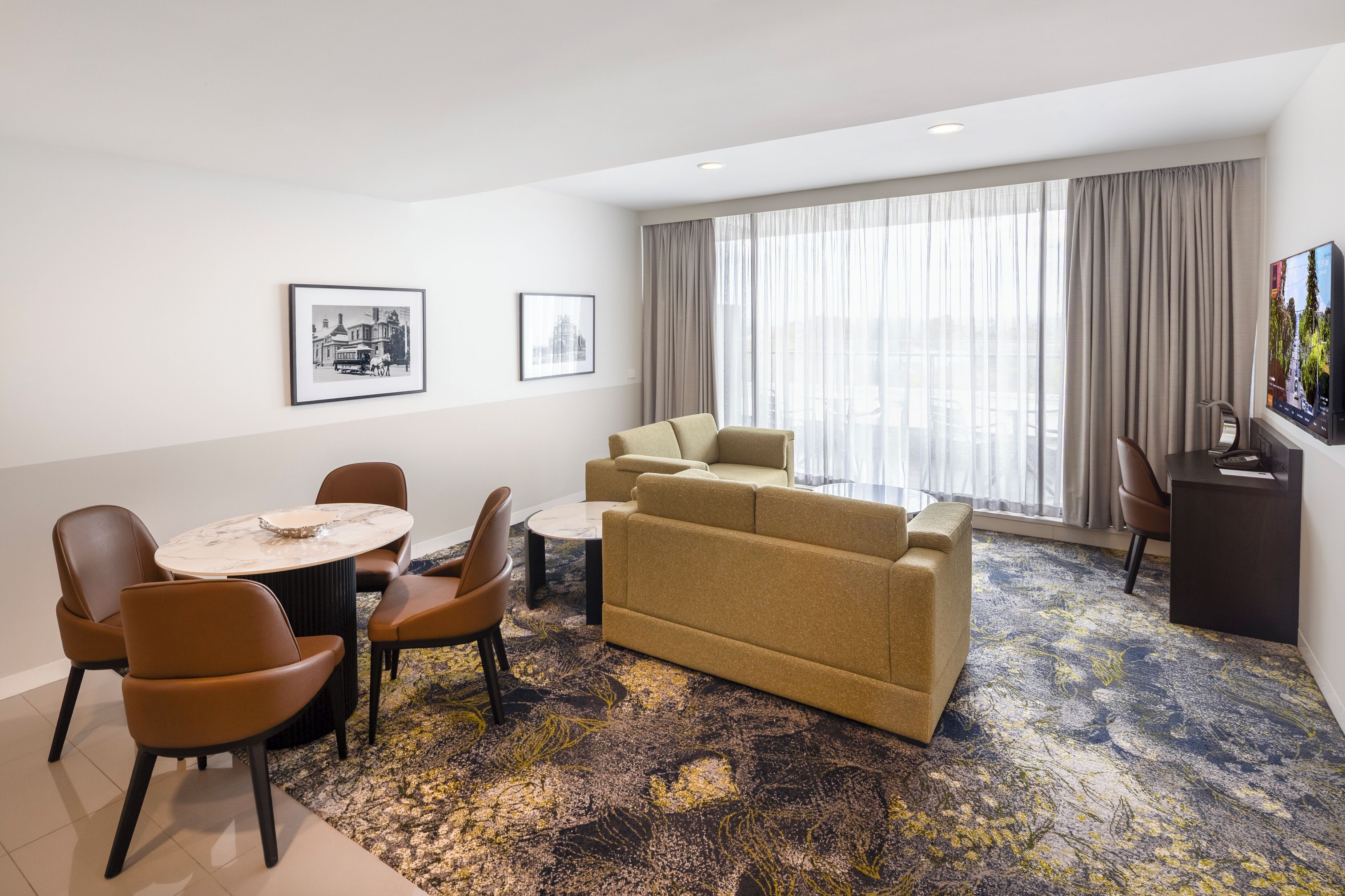 Habitación de hotel con comedor, sofá, televisión y obras de arte en las paredes.