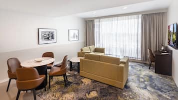 Habitación de hotel con comedor, sofá, televisión y obras de arte en las paredes.