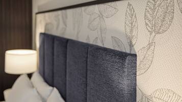 A headboard with a leaf pattern, a white lamp, and a dark-colored wall.
