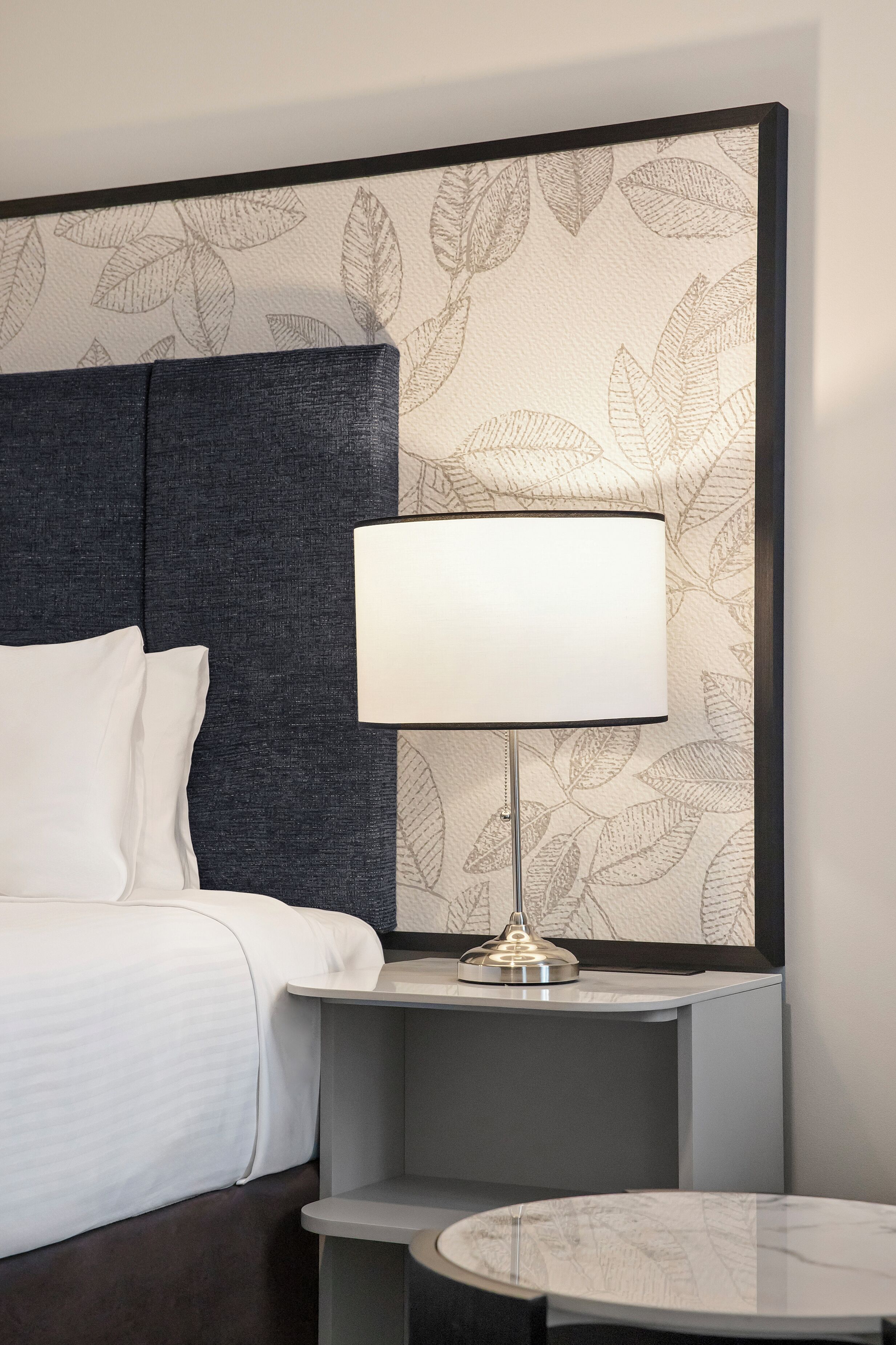 A hotel room with a bed, a bedside table with a lamp, and a small round table.