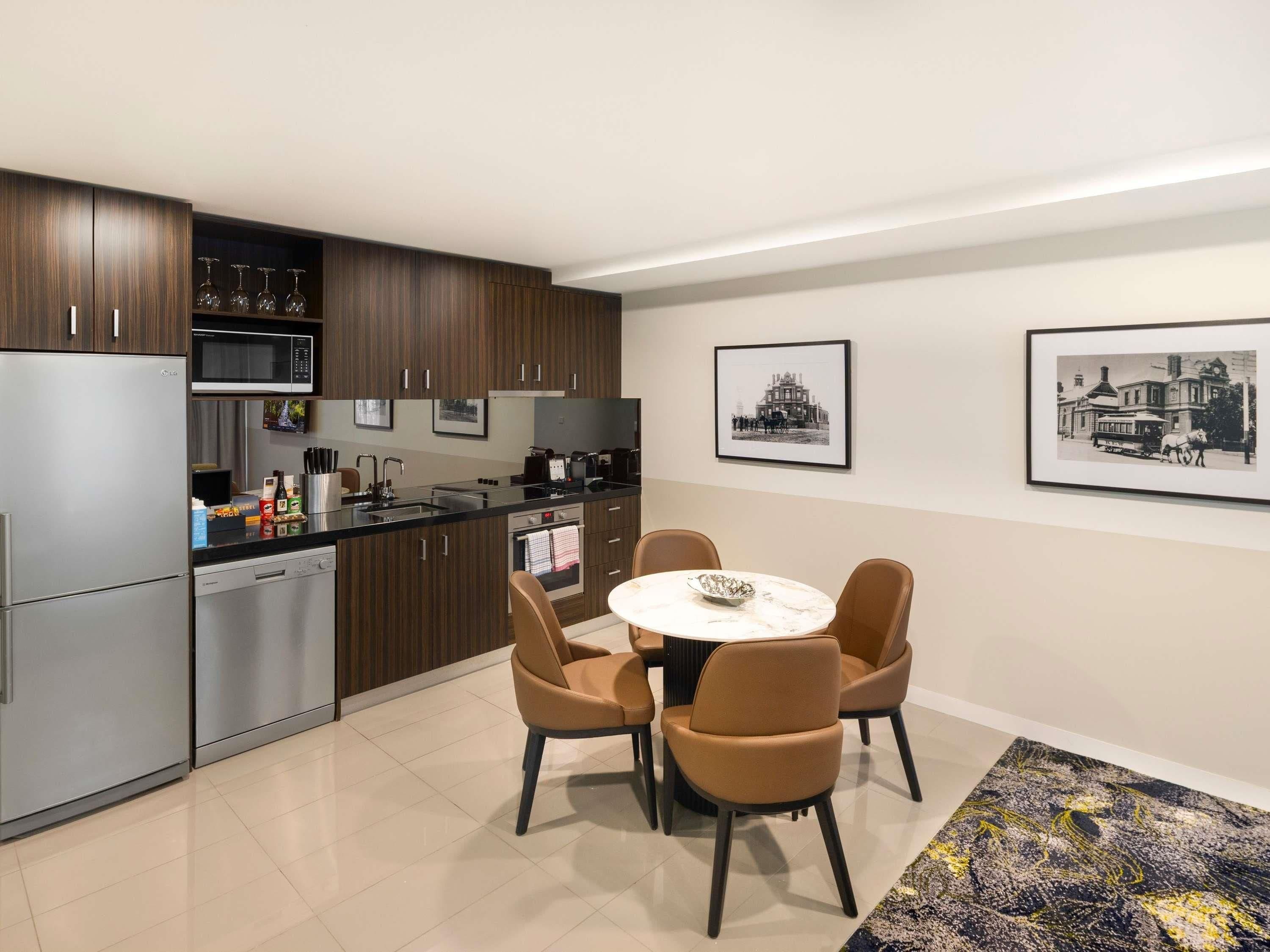 A modern kitchen with stainless steel appliances, a dining area with a round table and four chairs, and two framed photographs on the wall.