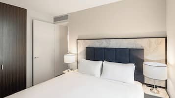 Una habitación de hotel con cama, dos lámparas de noche, cabecera con diseño de hojas, armario de madera y una puerta.