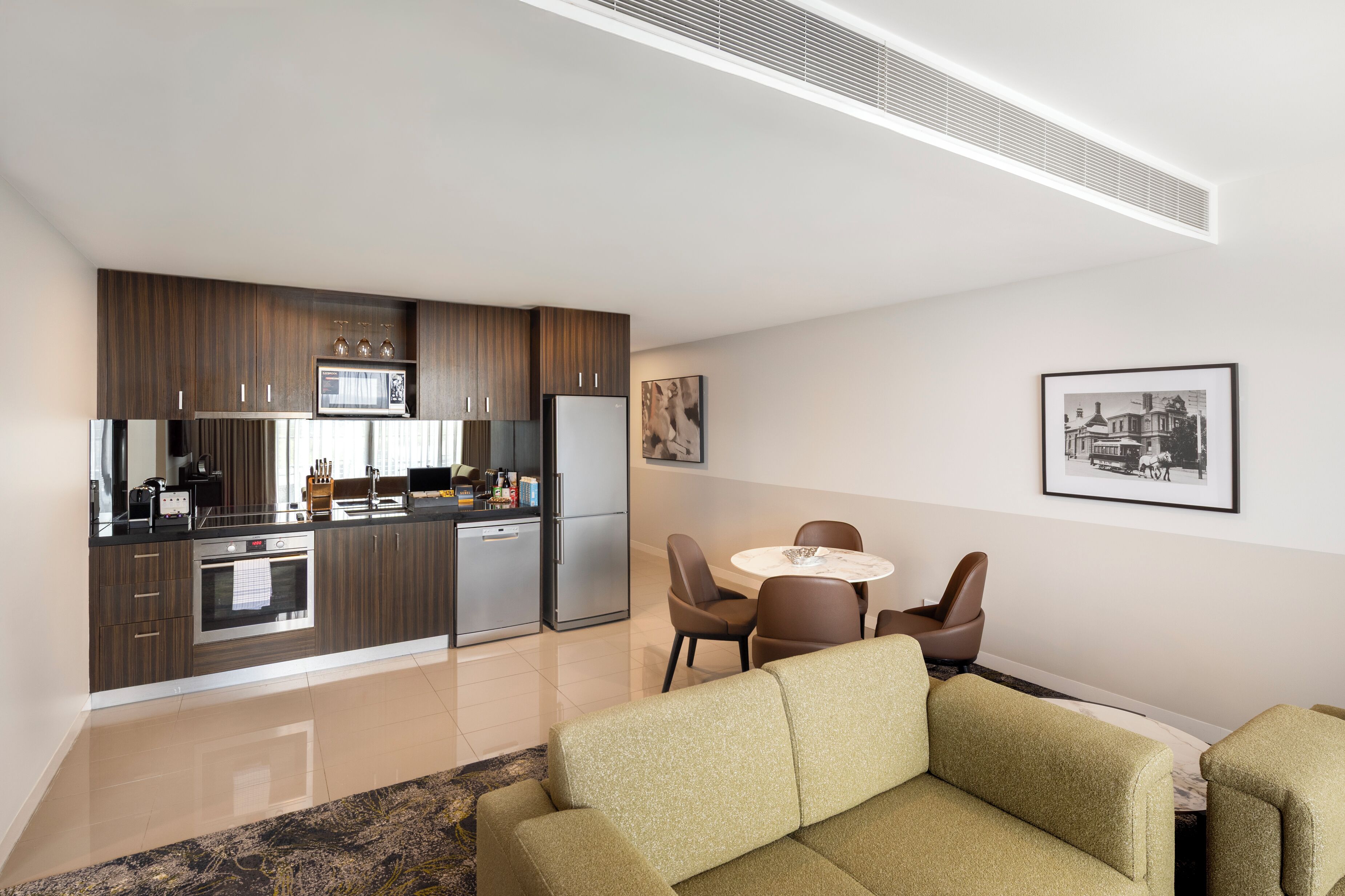 Une cuisine moderne dotée d’appareils électroménagers intégrés, un coin repas avec une table ronde et des chaises, et un canapé dans l’espace salon.