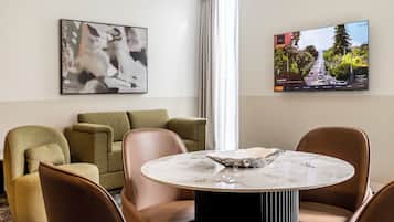 A modern living room with a round marble table, leather chairs, a green sofa, and two framed artworks on the walls.