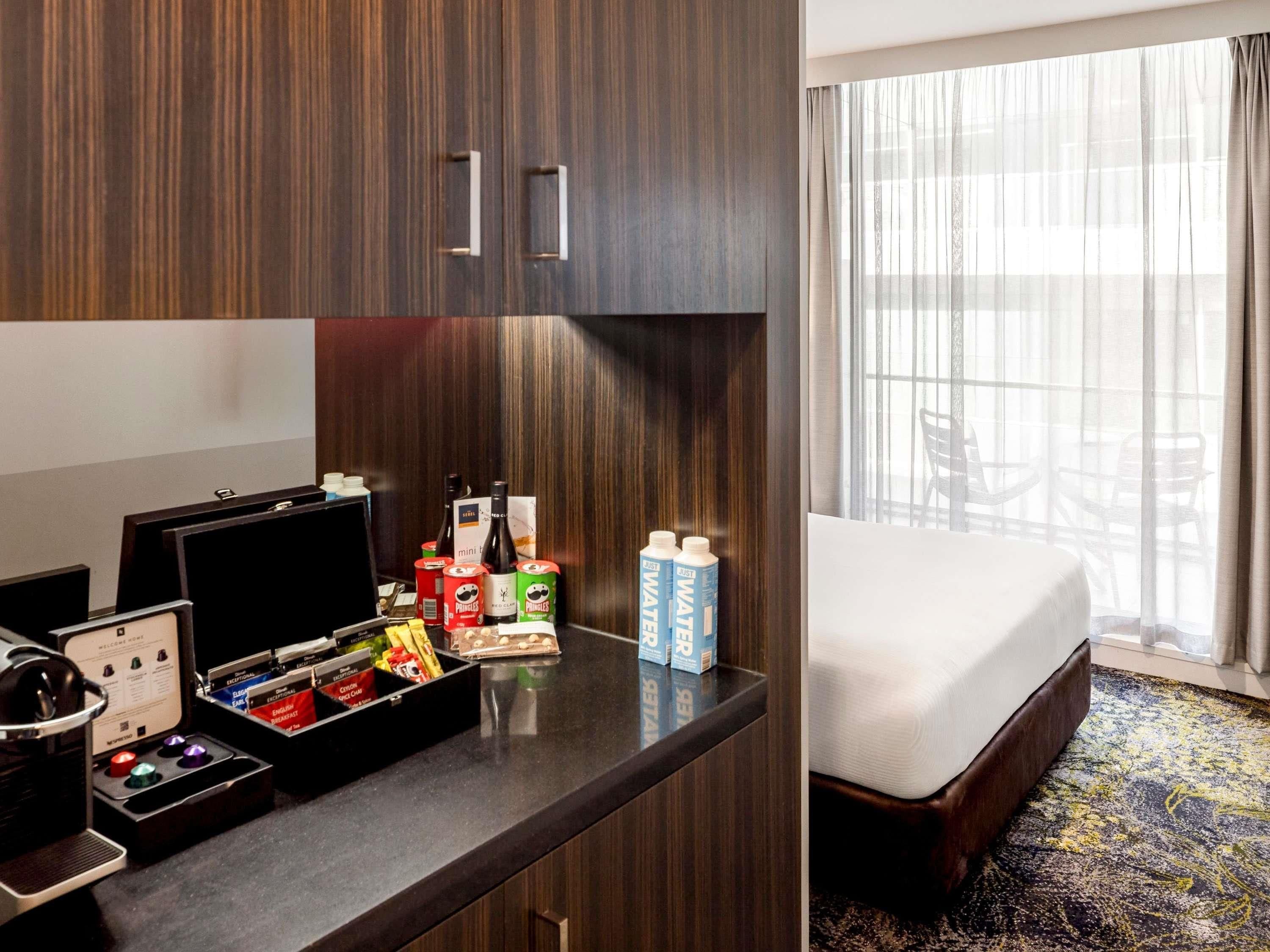 A hotel room with a bed, a desk with a laptop, a minibar, and a window with curtains.