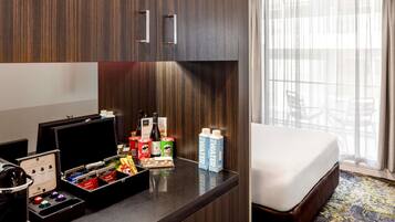 A hotel room with a bed, a desk with a laptop, a minibar, and a window with curtains.