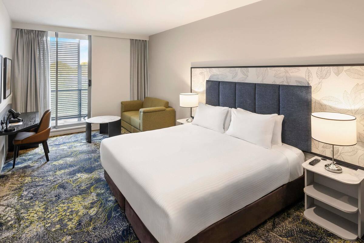 Una habitación de hotel con una cama grande, un escritorio con una silla, una mesita pequeña y una lámpara.