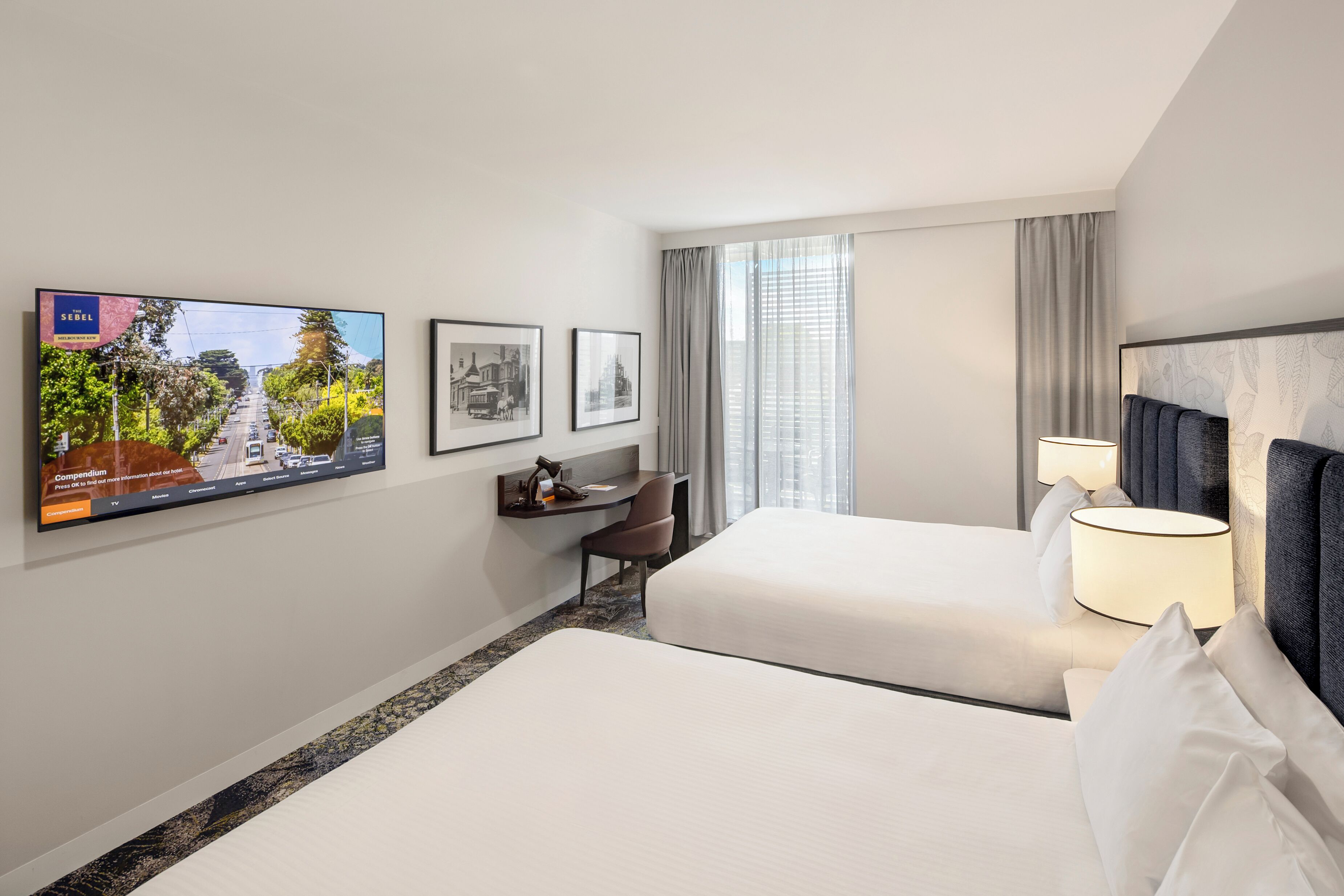 A hotel room with two beds, a desk, a chair, a TV, and a window with curtains.