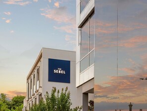 Un edificio moderno con un letrero que dice 'THE SEBEL' y un cielo despejado con nubes.
