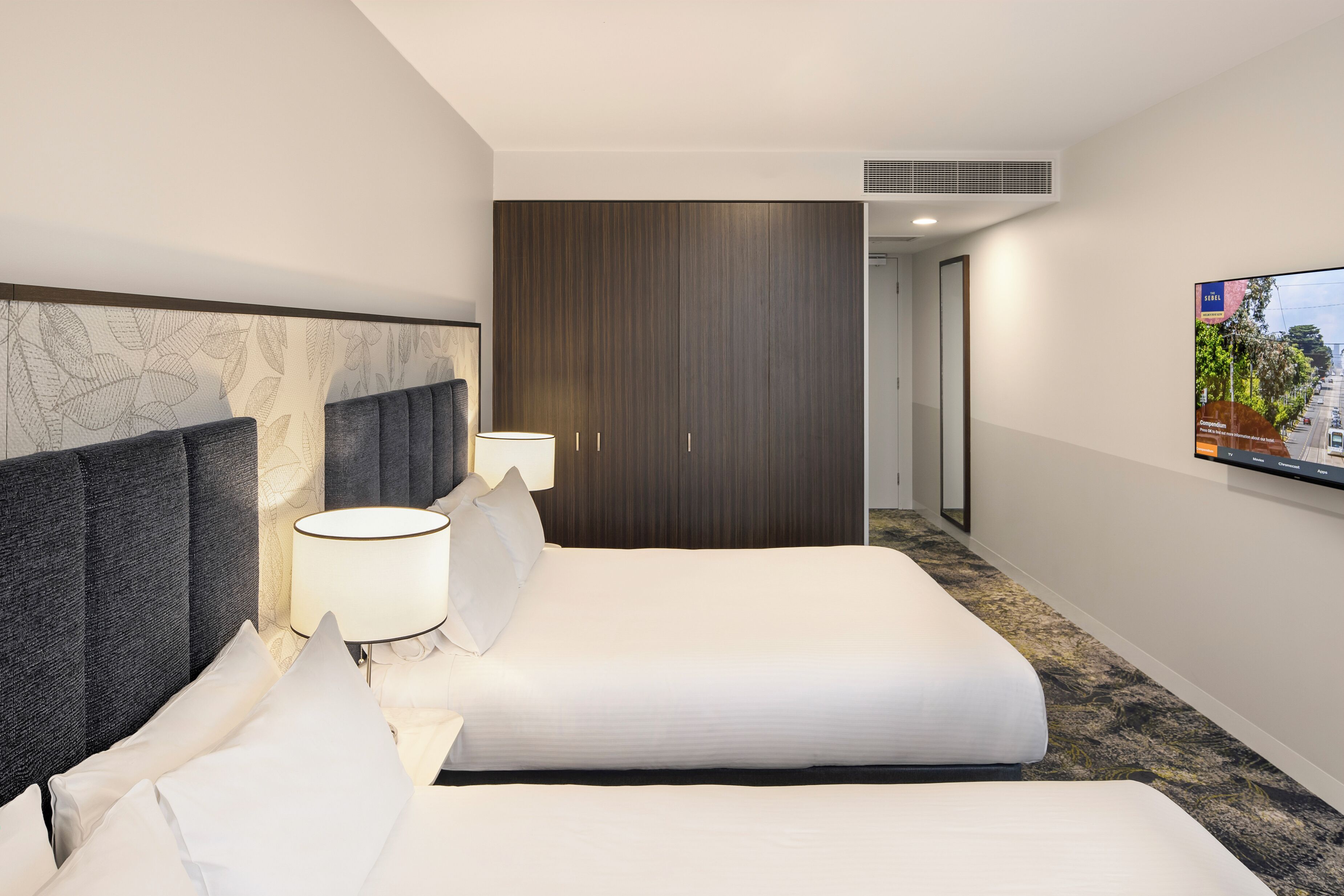 A hotel room with a large bed, a wardrobe, a TV, and a patterned wall.
