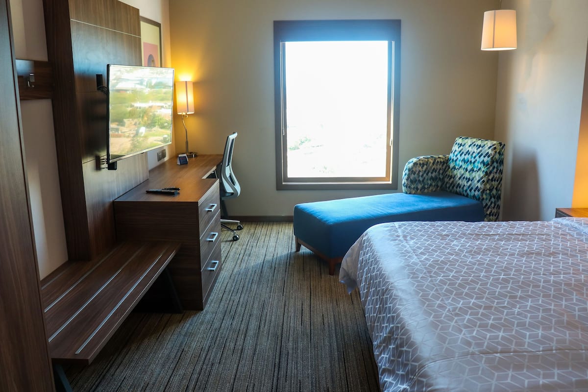 Habitación de hotel con cama, escritorio, televisor de pantalla plana, silla, ventana con vistas y lámpara.