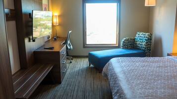 Habitación de hotel con cama, escritorio, televisor de pantalla plana, silla, ventana con vistas y lámpara.