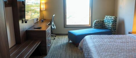 Une chambre d’hôtel avec un lit, un bureau, une chaise, une télévision et une fenêtre.