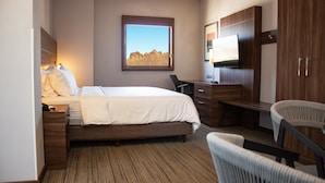 Une chambre d’hôtel avec un lit, un bureau, une chaise, une télévision et un tableau encadré au mur.