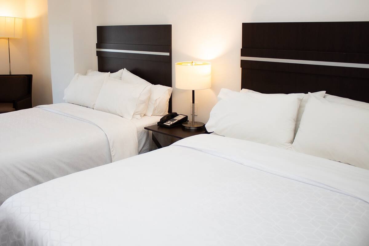Una habitación de hotel con dos camas, una silla, una mesita de noche con lámpara y un teléfono.