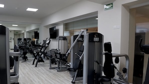 Une salle de sport équipée de divers appareils d’exercice, d’un téléviseur à écran plat et d’un panneau indiquant l’itinéraire d’évacuation.
