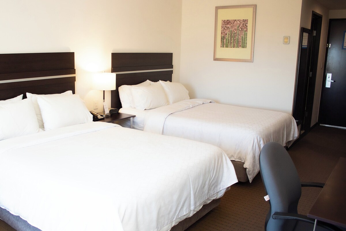 Quarto de hotel com duas camas, uma escrivaninha e uma cadeira.