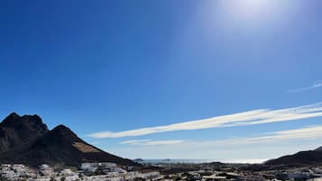 A coastal town with a prominent mountain in the background, clear skies, and a bright sun.