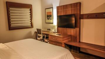 Habitación de hotel con cama, escritorio, silla, televisor y ventana con persianas.