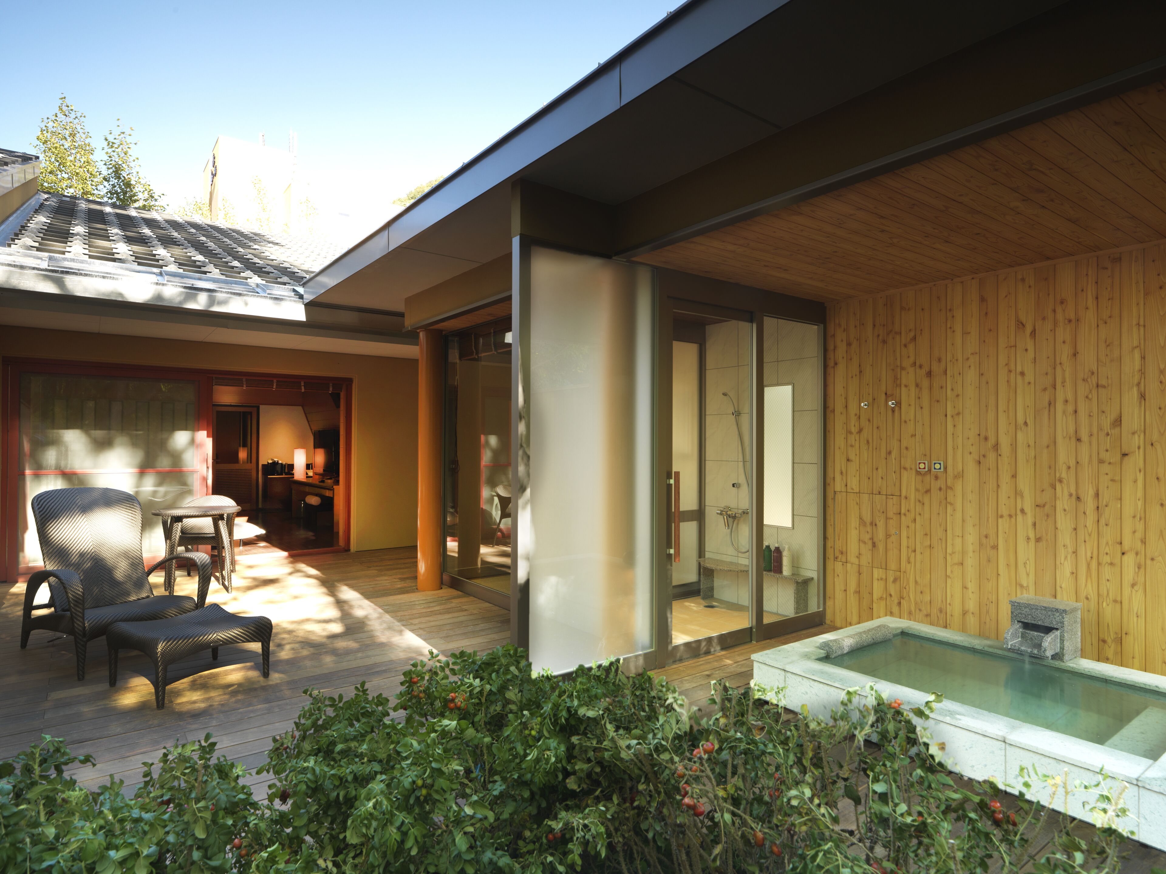 Een modern huis met een houten terras, een glazen douchecabine en een hottub.