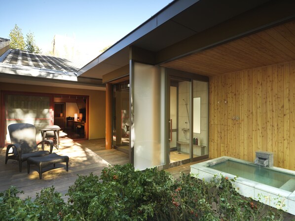 A modern house with a wooden deck, a glass-enclosed shower, and a hot tub.