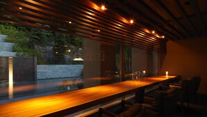 Eine moderne Bar mit einer langen Theke, Holzhängern an der Decke und Blick auf ein Wasserelement im Außenbereich.
