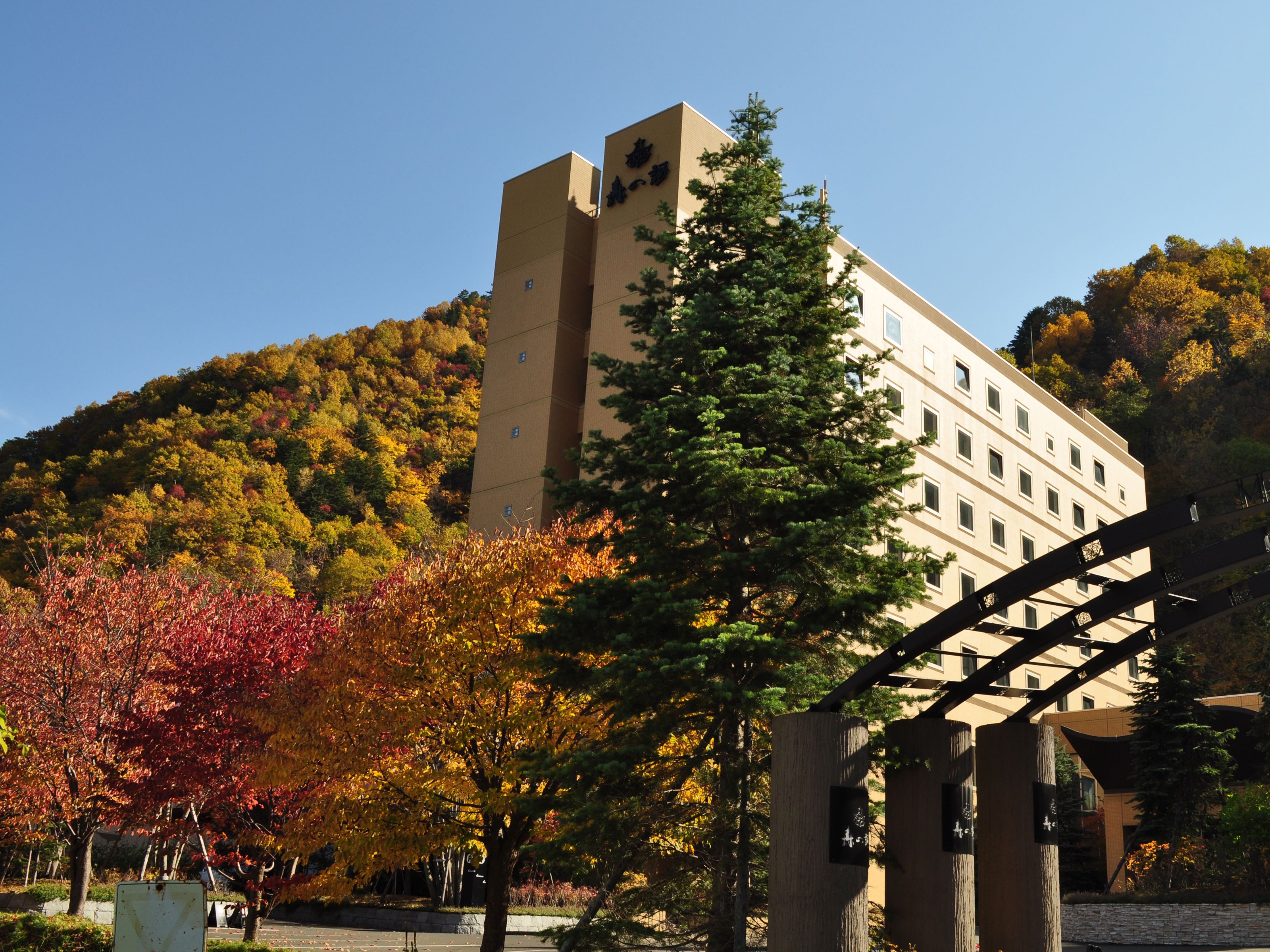 Ein Gebäude mit einem Turm und zahlreichen Fenstern, umgeben von Bäumen in Herbstfarben.