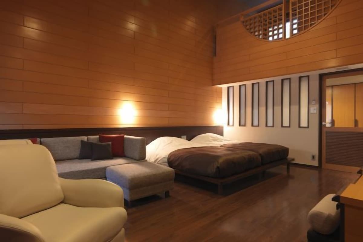 A modern hotel room with a wooden floor, a sofa, a bed, and a small table.